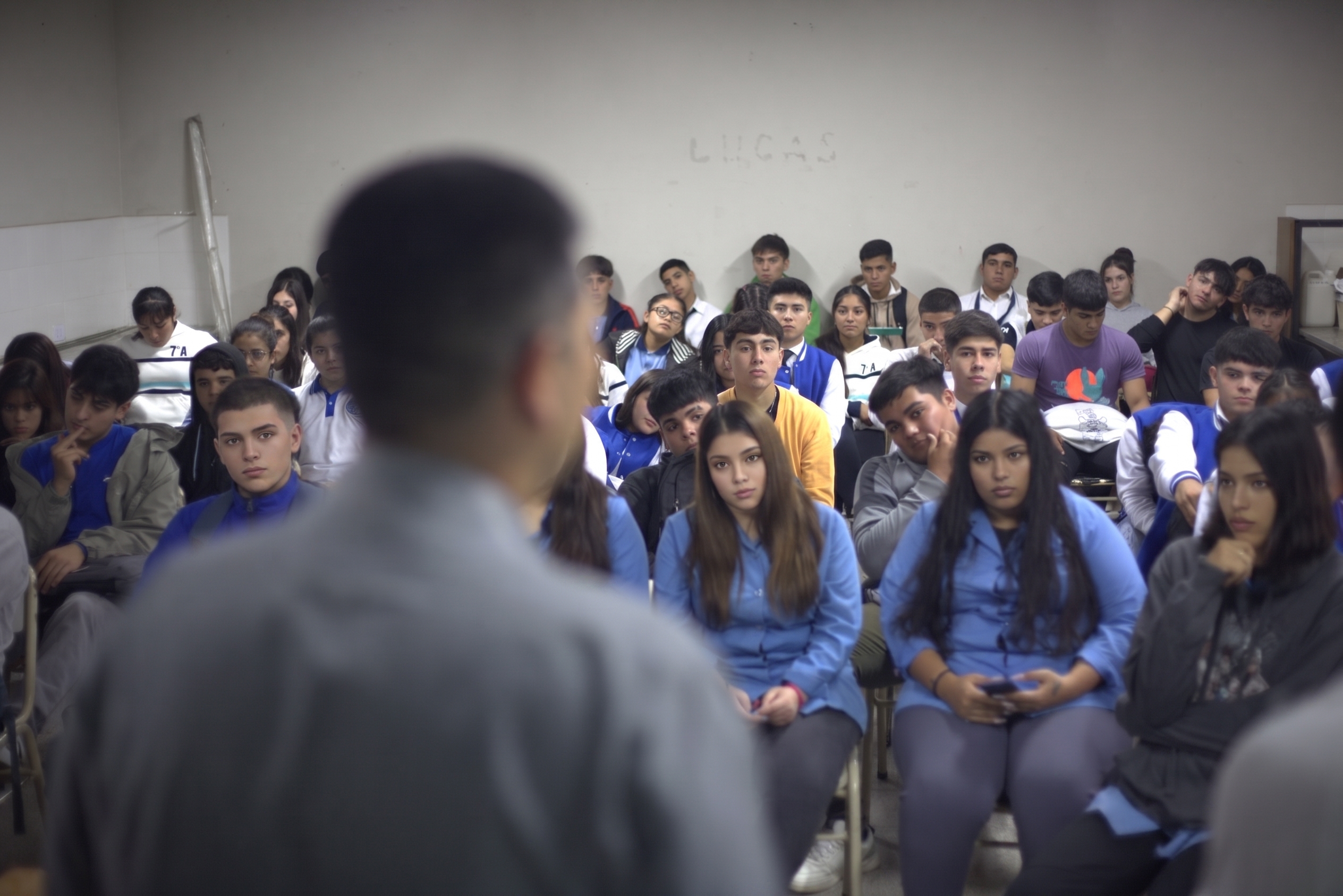 Estudiantes escuchando un taller de prevención en un aula, de espaldas a un coordinador
